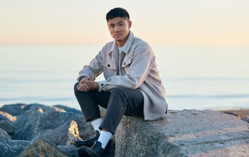 Man sitting on on rocks at beach at golden hour looking at camera Man sitting on on rocks at beach at golden hour looking at camera